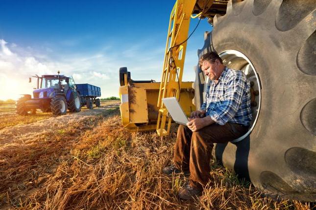 Man sitting next to farm equipment and working on a laptop.